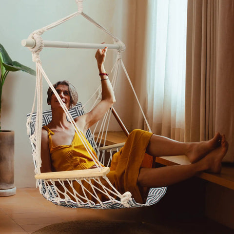 Person relaxing in an upgraded hammock chair with wooden armrests and steel spreader bar, cotton woven fabric, indoor use.