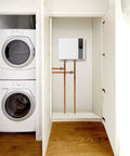 Score Instant Hot Water With This Beast-Mode 26.9 KW Electric Tankless Water Heater mounted beside a stacked washer and dryer.