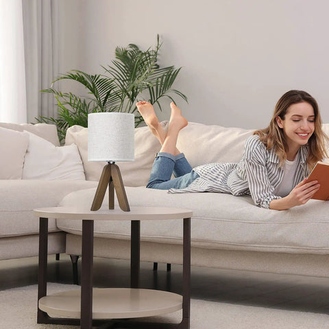 Wooden Tripod Table Lamp With Brown Base And Linen Fabric Shade, Space Saving Nightstand Light For Bedroom next to a woman reading