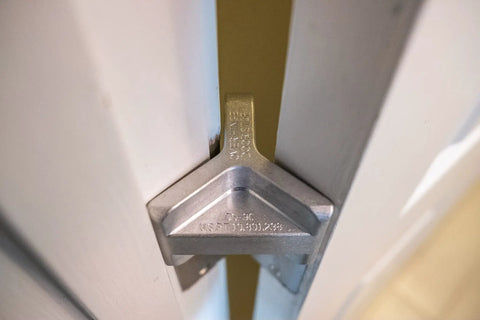 Patented Safety Bar Door Stop for Tension Hinged Doors in metal installed on a door, holds door secure at 90-degree angle without damage.