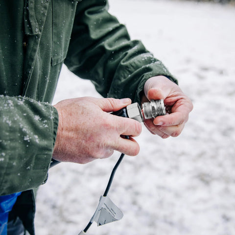 Camco 25-ft heated RV water hose connector, close-up of hands attaching in snow; metal threaded ends visible