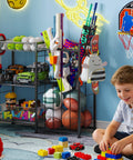 All In One Sports Gear Organizer Cart With Elastic Straps And Removable Basket For Garage Organization, Ball Storage Rack For Basketballs Soccer Balls And More, Hooks For Toy Gear Storage, Black holding sports balls, toy cars, and gear in playroom.