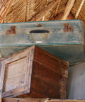 Stacked vintage suitcase with old wooden crate and thatched roof in background