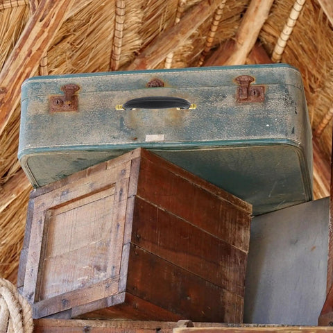 Stacked vintage suitcase with old wooden crate and thatched roof in background