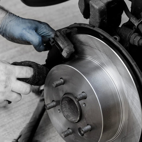 Brake rotor close-up: steel disc with hub and lug studs being serviced by gloved hands.