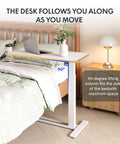 32 Inch Mobile Standing Desk Featuring A Slick Rolling Base And Hassle Free Pneumatic Height Adjustments With Smooth One Hand Gas Spring Lift For Compact Home Office Computer Workstation Setup beside a bed with laptop.