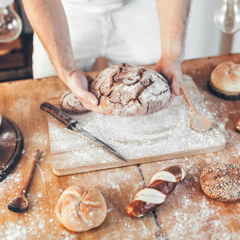 Baker holding bread with Double Acting Baking Powder In A Resealable Bucket For Cookies Cakes Muffins Biscuits And Pancakes.