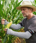 Man wearing cut resistant arm sleeves with thumb holes adjustable 18 inch grey protection in cornfield for yard work