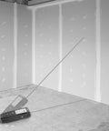 Micro Laser Distance Meter With Bluetooth Sync And Tilt Sensor measuring in a room with unfinished drywall walls.