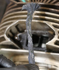 Gloved hand holding Non Metallic Anti Seize Lubricant For Threads Surviving Extreme Heat And Cold, Water Resistant Military Grade Formula With Rust And Corrosion Inhibitors, Sulfur Lead Copper Free, Delivers Controlled Friction And Torque For Hydraulic Efficiency, Half Pound jar near machinery.