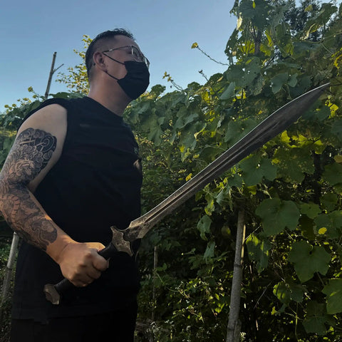 Person holding Hand Forged Knight Sword in Spring Steel 35 Inch Full Tang Medieval Blade outdoors near greenery