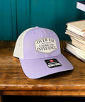 Over Par And Under The Influence Golf Trucker Hat For Women With Dimpled Ball Patch Purple Lilac Birch Color 6 Panel Structured Richardson 115 Cap Funny Golf Accessory displayed on wooden surface