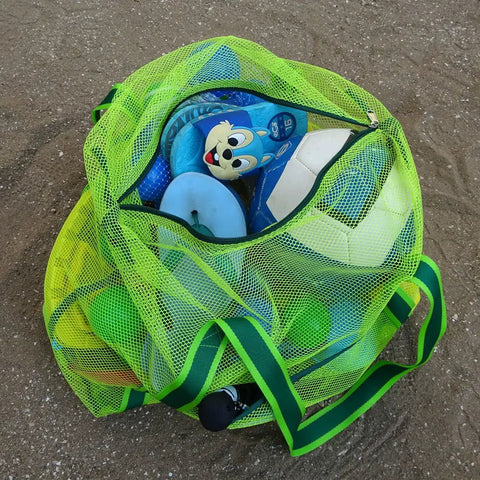 Green Must-Have Mesh Beach Toy Bag With Zipper Top, full of toys, on sandy ground, ideal for quick dry and easy carry. 