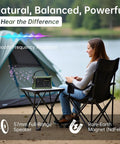 Woman sitting by tent with Emergency Solar Radio With Hand Crank And 12000mAh Battery Pack on table, lake in background.