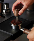 Pro 58 Mm Espresso Powder Distributor With Tough Walnut Handle And Stainless Steel Tines in use on coffee grounds.