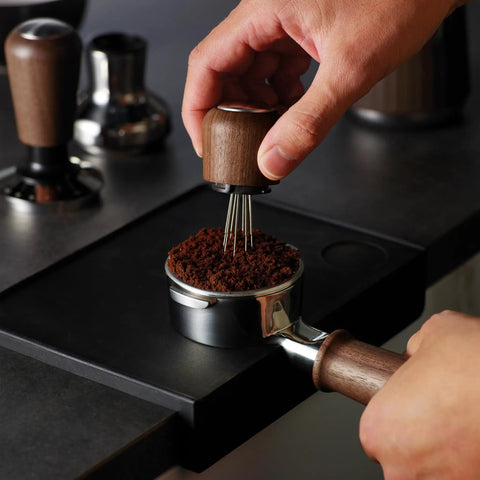 Pro 58 Mm Espresso Powder Distributor With Tough Walnut Handle And Stainless Steel Tines in use on coffee grounds.