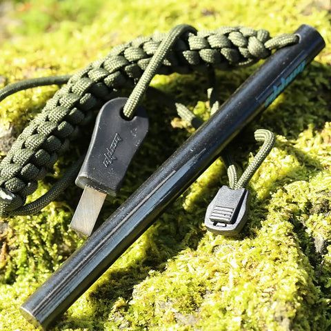 Survival Fire Starter Kit With Drilled Ferrocerium Rod Half Inch By Six Inch Striker Pro on moss with paracord lanyard.