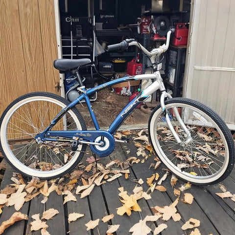 Blue comfort bike with white tires beside a shed on a wooden platform surrounded by fallen leaves