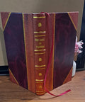 Front view of burgundy leather-bound book with gold tooling, in a maroon case with purple side panels and red ribbon