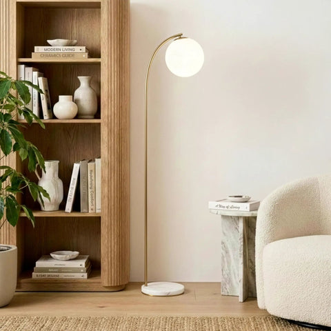 Luna Drop 75 Inch Antique Brass Floor Lamp With Frosted White Glass Globe Shade in a cozy living room corner with bookshelves.