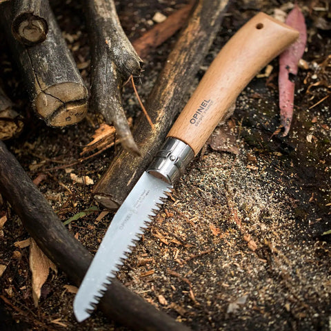 Badass Lightweight Folding Saw For Weekend Campouts And Garden Grind Cuts Branches Fast With Razor Sharp Carbon Steel Blade Secure Virobloc Lock And Natural Beechwood Handle on wooden ground with sticks.