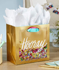 Medium Gift Bag With Tissue Paper And Hooray Confetti Design In Gold With Pink Teal Purple For Bridal Showers Graduations Retirements And More The Perfect Gift Wrap On The Go 7.75 Inch Gift Bag displayed on a desk with stationery.