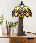 Irish Celtic Tiffany Style Stained Glass Table Lamp With 17500 Lumen Light, bronze metal base on wooden desk with plants.