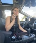 Woman in car using phone with Hella Quick Retractable Car Charger Featuring Four USB C Ports And 120 Watt Output for fast charging.
