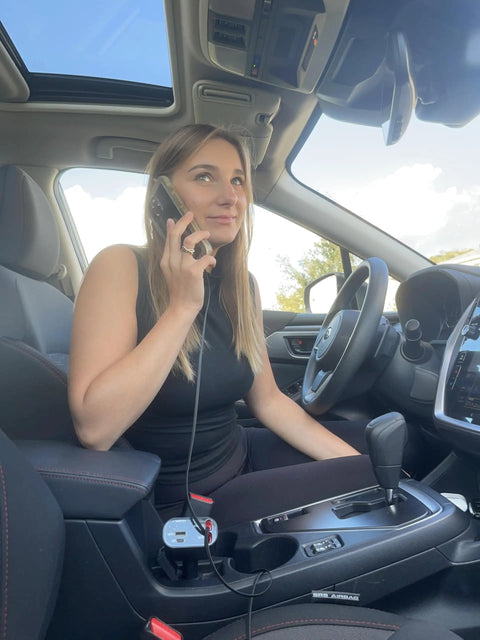 Woman in car using phone with Hella Quick Retractable Car Charger Featuring Four USB C Ports And 120 Watt Output for fast charging.
