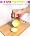 Joie crinkle cutter knife with red handle and stainless steel wavy blade slicing a green apple on a cutting board.
