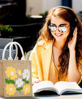 Woman reading outdoors with Beginner Punch Needle Kit With Tote Bag, featuring floral design in yellow and white on the table.