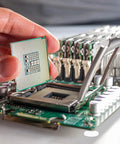Close-up of a hand placing a CPU on a motherboard with various electronic components and standoffs surrounding.