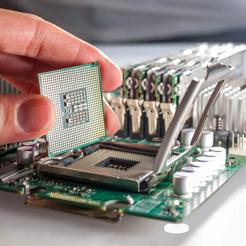 Close-up of a hand placing a CPU on a motherboard with various electronic components and standoffs surrounding.