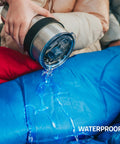 Person pouring water on blue waterproof All Season Sleeping Bag For Adults And Kids, Lightweight And Cozy Waterproof Gear For Backpacking Camping And Hiking, Temperature Rated 50F To 77F, Fits 6ft Adults, Single Or Double Comfort, Must Have Outdoor Sleep Gear