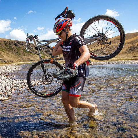 Cyclist carrying a bike across a shallow stream