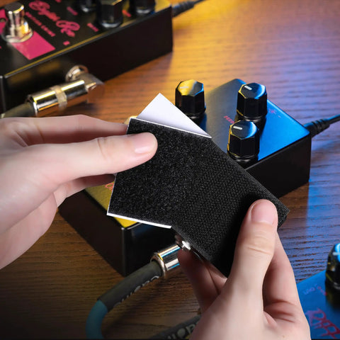 Hands applying Heavy Duty Guitar Pedalboard Mounting Tape With Adhesive Hook And Loop Strips Keeps Effects Pedals Secure On Your Board