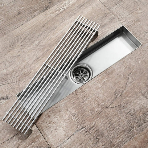 Slick Linear Shower Drain With A Heavy Duty Removable Cover Grate Plus Odor Locking Trap Built From Top Shelf 304 Stainless Steel on wooden floor.
