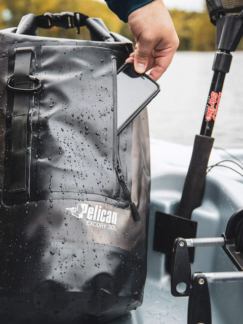 Person placing phone in ExoDry 30L Large Drybag With Roll Top Closure Waterproof 500D PVC on boat, showcasing waterproof feature.