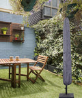 Patio Umbrella Cover With Rod For 7 To 11 Foot And 15 Foot Double Sided Umbrellas Built Tough With 600D Oxford Fabric Waterproof Zippered Weatherproof Gray covering an umbrella in a garden setting.