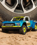 Grom 4x4 Desert RC Truck Ready To Run With Battery And Charger Included 2S LiPo Smart Charger All Terrain Enclosed Metal Gear Drivetrain Beefy V2 Differentials Clipless Body Mojave Style Blue White on sand next to tire