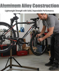 Man using Lightweight Aluminum Bike Repair Stand Portable Work Stand For Mountain MTB And Road Bikes Height Adjustable From 39 To 59 Inches Holds Up To 55 Lbs For DIY Home Garage Use in garage
