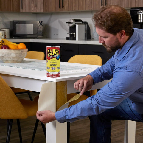 Man using Thick Rubberized Waterproof Tape That Seals Leaks Fast And Holds Up Under Water Flexible Patch For Indoor Outdoor Repairs On Roofs Plumbing Pool And More White 12 Inch By 10 Foot Pack Of 1 to repair table leg in kitchen.