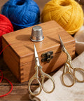 Stainless Steel Embroidery Scissors Set 2 Pcs 3.6 Inch Gold Tone Small Shears For Sewing Crafting Needlework Thread Cutting Premium Quality Durable Anti Rust Pointed Tip Pro Grade Essentials beside a wooden box with colorful yarn.