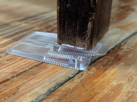 Kick Those Wobbles To The Curb With This Solid Thirty Four Piece Plastic Shim Kit using a clear shim under a wooden furniture leg.