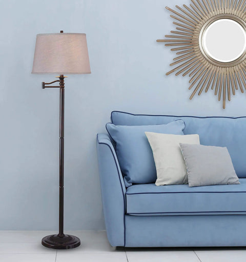 Riverside Copper Bronze Swing Arm Floor Lamp With Cozy Warm Glow Oatmeal Drum Shade next to a blue sofa and sunburst mirror.