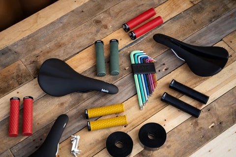 Assorted bike accessories including seats, grips, and tools on a wooden surface, excluding Pocket-Ready Aluminum Chain Splitter.