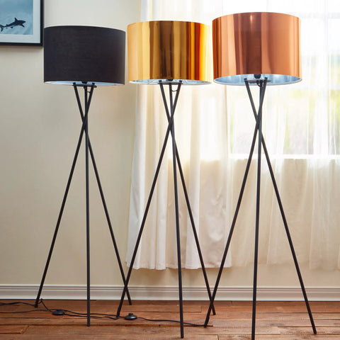 Three modern tripod floor lamps with copper drum shades in black metal finish in a living room, showcasing soft ambient glow.