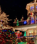 Festive house decorated with multicolored Christmas lights, featuring illuminated trees and ornaments, at night.