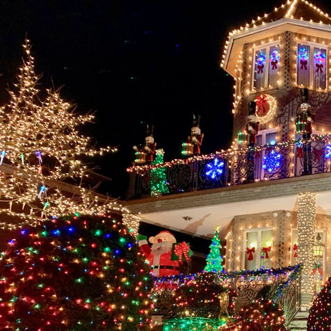 Festive house decorated with multicolored Christmas lights, featuring illuminated trees and ornaments, at night.