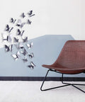 3D Mirror Butterfly Wall Decor Kit With 48 Removable Stickers in Silver Finish displayed above a chair on a wall